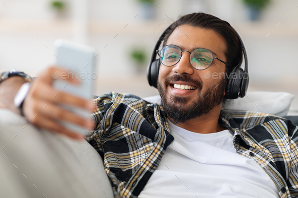 Handsome arab guy watching movie, using wireless headset and cellphone