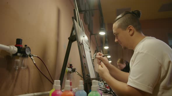 Man Artist Learns to Paint with Airbrush with Acrylic Dye Paper and Easel alt