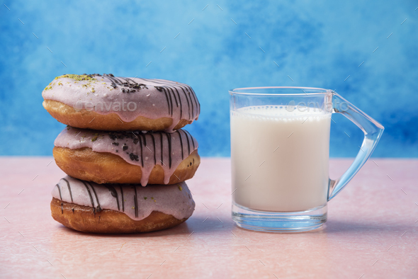 Stack of strawberry donuts and a glass of milk on pink table