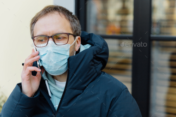 Sad man in panic because of epidemic disease, covers face with medical mask