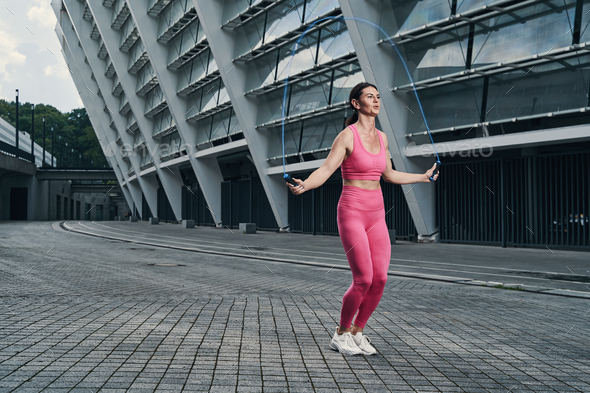 Woman skipping with jump rope outside of building Stock Photo by Iakobchuk