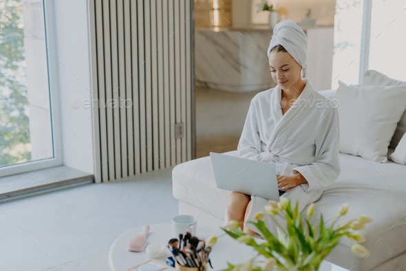Attractive female model wears bathrobe and towel types on laptop computer