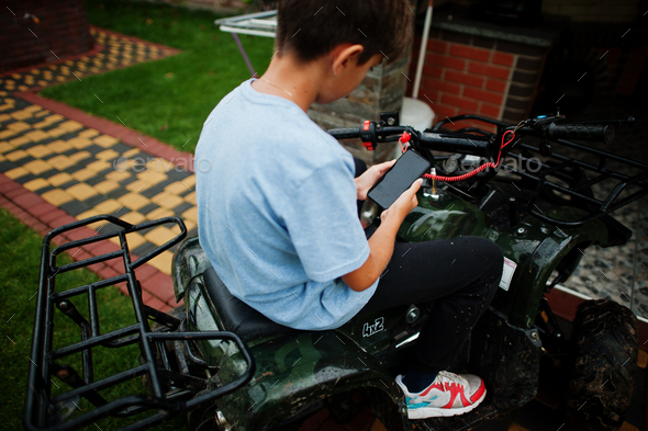 Boy in four-wheller ATV quad bike with mobile phone. - Stock Photo - Images