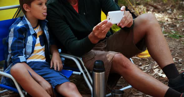 Father and son taking a selfie on mobile phone outside tent alt