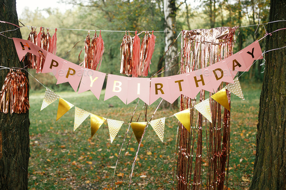 Stylish birthday garland hanging in park. Modern rose gold tassel garland and happy birthday banner
