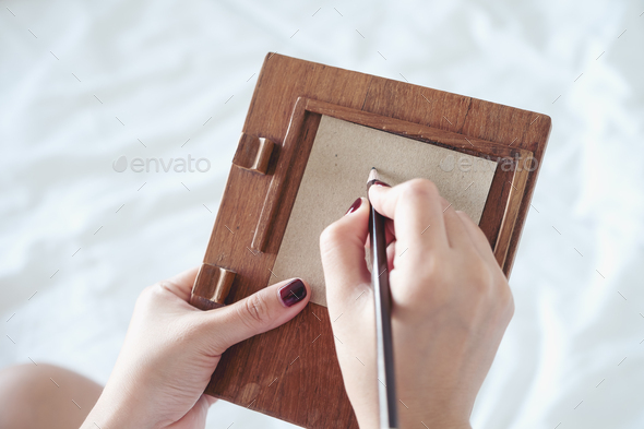 A woman writing on a brown paper with wooden writing pad on the bed