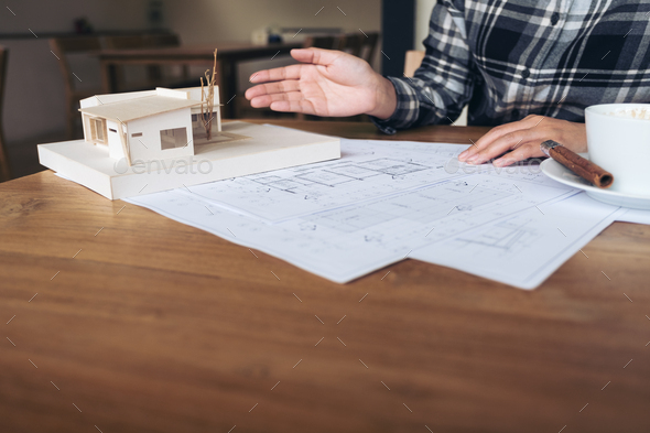An architect working on an architecture model with shop drawing paper and coffee cup on table