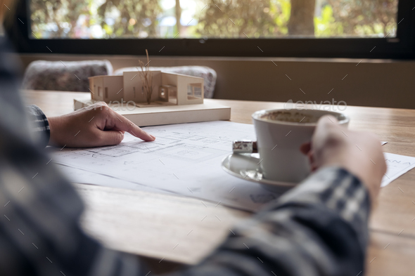 An architect working on an architecture model with shop drawing paper while drinking coffee