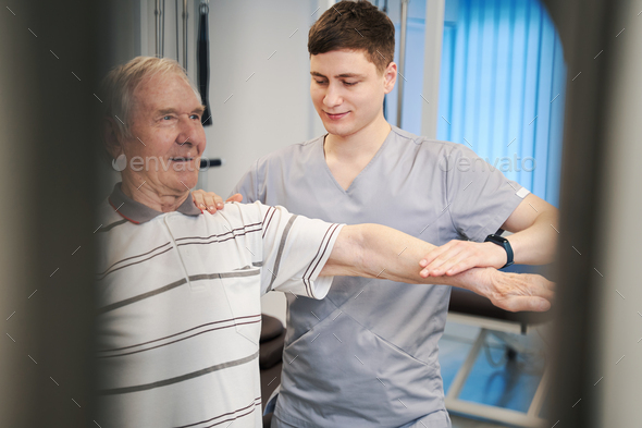 Physiotherapist assisting in training of aged man left arm