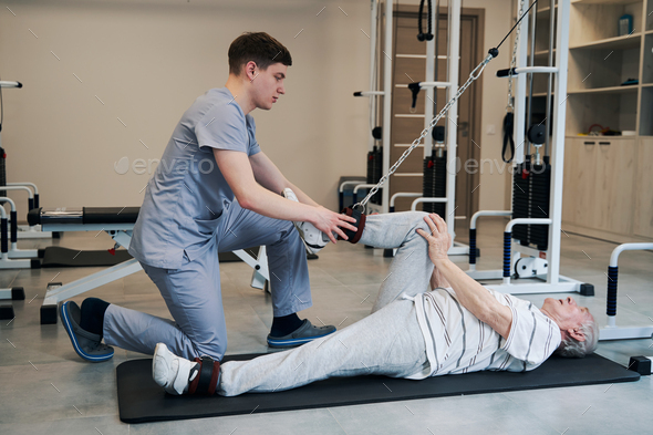 Retired man bending knee with attached rope of rehabilitation equipment ...