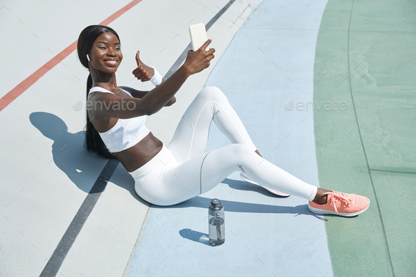 Beautiful young African woman in sports clothing having video call and smiling
