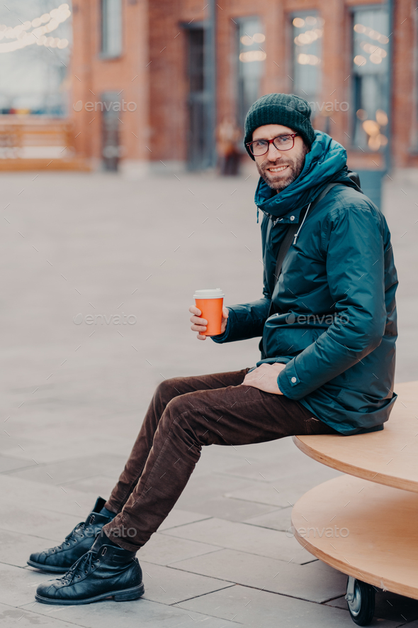 Winter fashion concept. Guy enjoy sunny winter day. Hipster walk snowy  winter day. Snowflakes in air on bright winter day. Man unshaven wear warm  jacket with fur and scarf snowy nature background