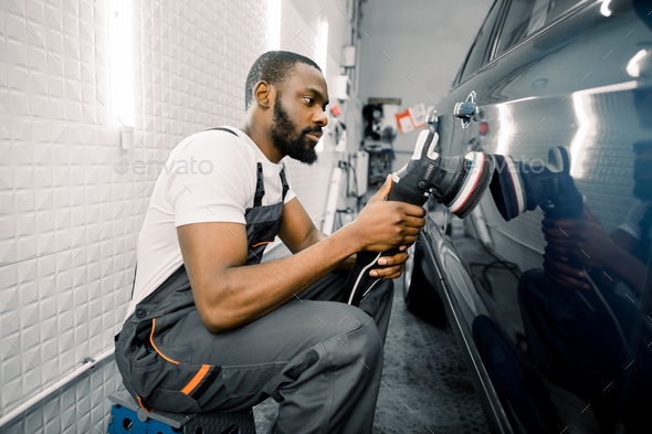 Auto detailing service, polishing of the car. Side view of young African American man worker n t