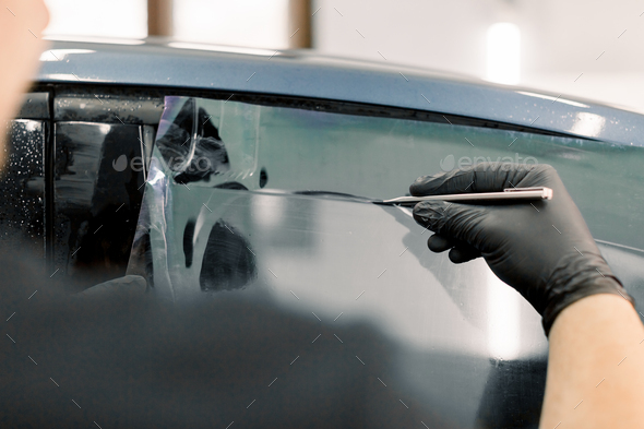 Cropped image of hands of worker in garage tinting a car window with tinted foil or film, holding - Stock Photo - Images