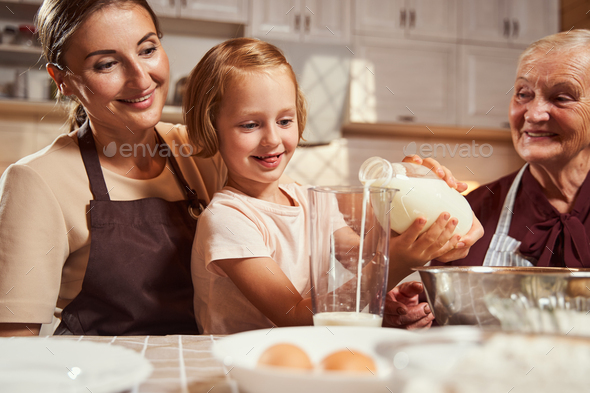 Proud mother and granny looking at child pouring milk Stock Photo by ...