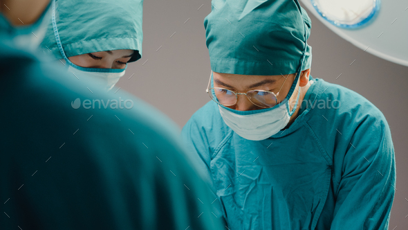 Young Asian assistants and nurses performing invasive surgery on patient in hospital operating room. - Stock Photo - Images
