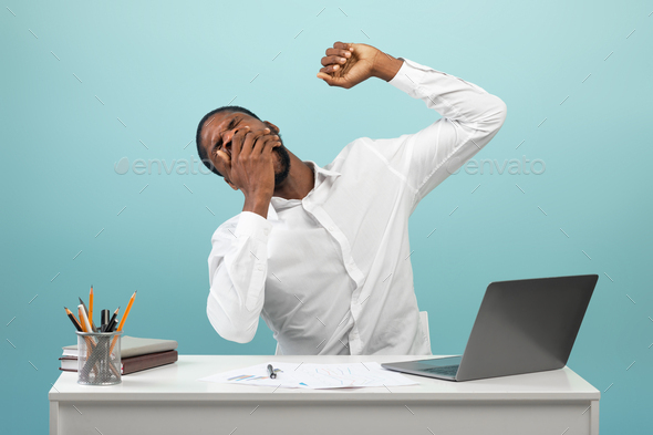 African american businessman yawning and stretching hands, looking sleepy, sitting at workplace