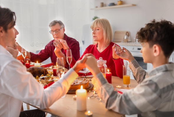 Religious extended family holding hands and praying before festive Christmas or Thanksgiving dinner