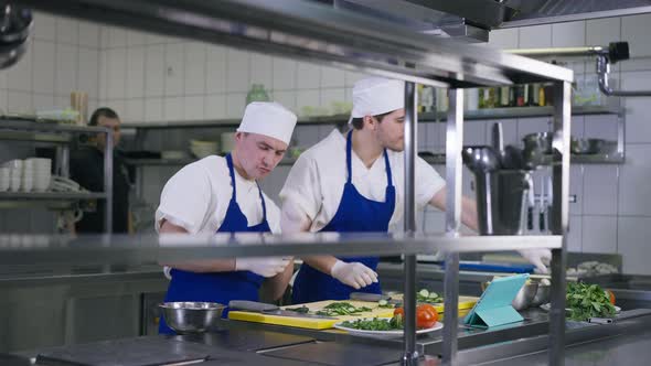Two Joyful Cooks Having Fun Dancing in Kitchen As Chef Passing at Background and Employees Calming alt