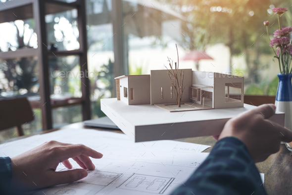 An architect working and holding an architecture model with shop drawing paper on table