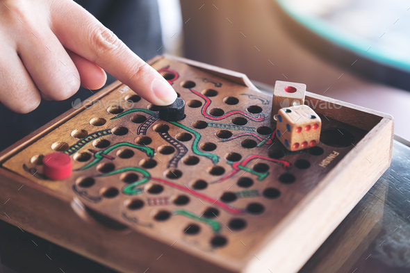 Closeup image of a hand playing wooden Snakes and Ladders game