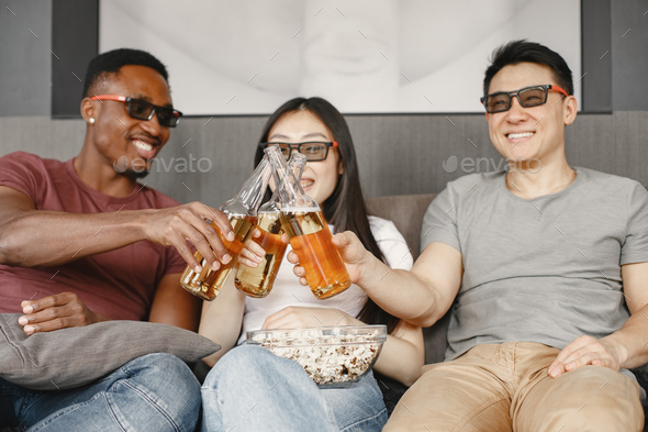 Three friends clink a bottles with beer, watching film