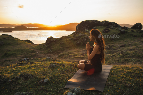 Woman doing yoga alone at sunrise with mountain and ocean view. Harmony with nature