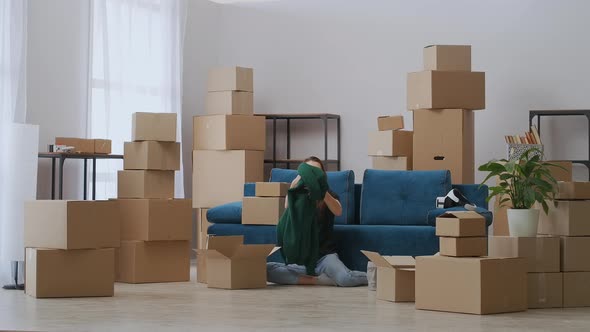 A Young Girl is Sitting on the Floor Near the Sofa Packing for the Move alt