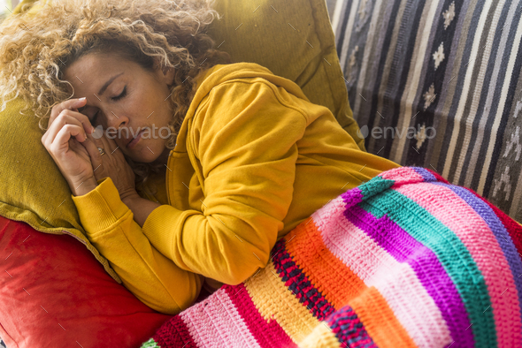 Tired woman sleep by day on the sofa with colorful cover - stress and sunday time indoor