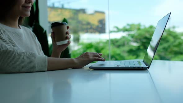 Closeup a woman drinking coffee while working and touching on laptop computer touchpad