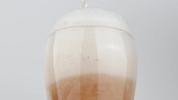 Pouring lager beer in glass over white background, low angle view alt
