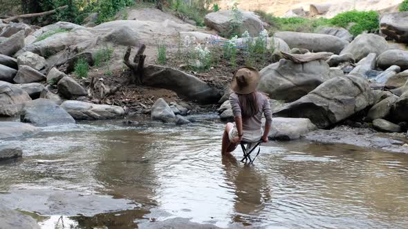 Rear view of a young Asian woman sitting and relaxing on a chair in waterfall stream