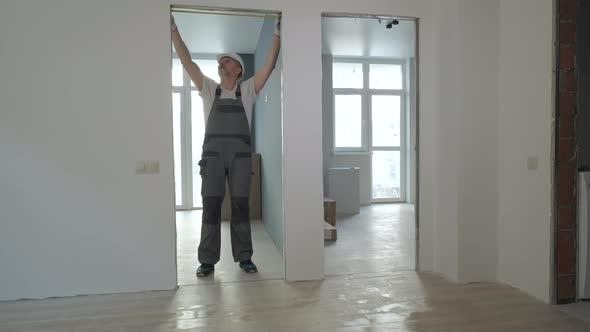 A Builder in Working Uniform Checks the Size and Quality of Doorways in a New Apartment alt