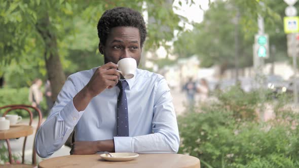 African Businessman Drinking Coffee while Sitting in Outdoor Cafe alt