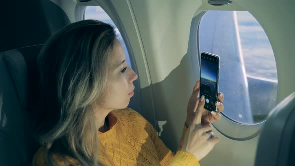 A Woman Is Taking Pictures with Her Cellphone During Her Flight alt