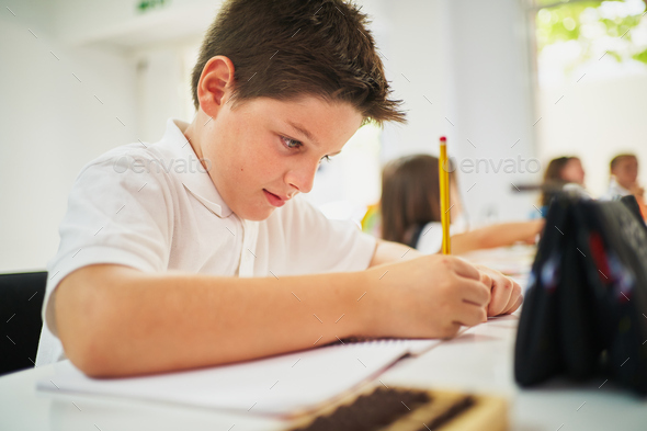 Young spanish boy writing on notebook with pencil at class