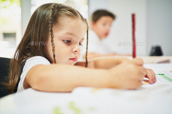 Young spanish girl writing on notebook with pencil at class