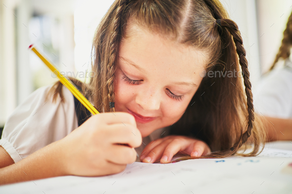 Young spanish girl writing on notebook with pencil at class