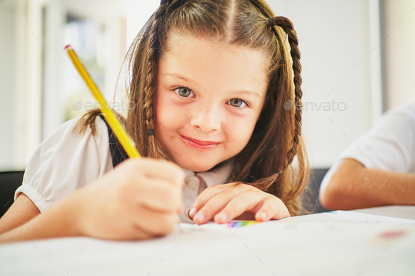 Young spanish girl writing on notebook with pencil at class looking at camera