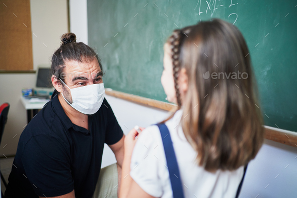 Spanish teacher wearing mask shows to student girl how to make exercise