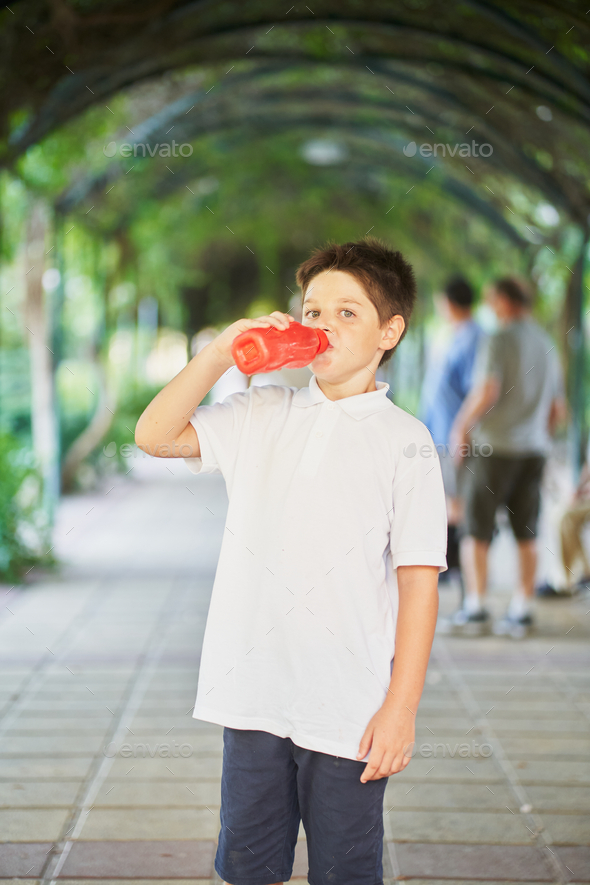 Spanish little boy drinking water from a red bottle in park Stock Photo