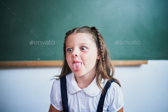 Little spanish school girl sticking out tongue against class chalkboard