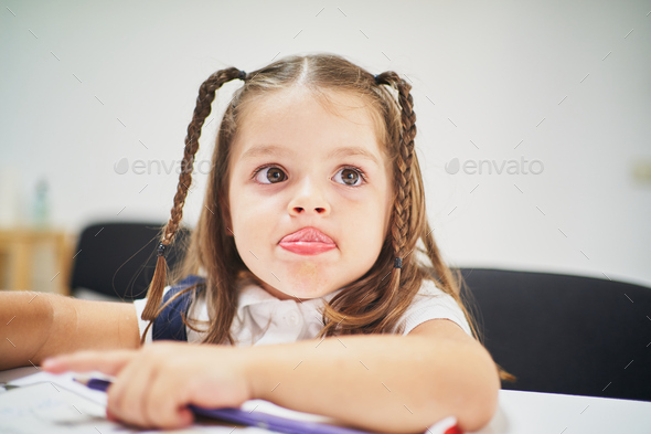 Young little spanish girl sticking out tongue in class