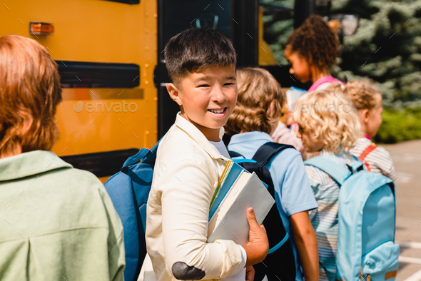 Chinese korean asian schoolboy pupil standing in line with his classmates for boarding school bus