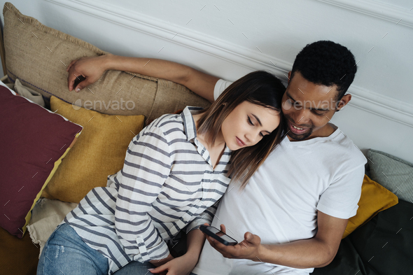 Mixed race couple relax on couch in living room watch movie on smartphone - Stock Photo - Images