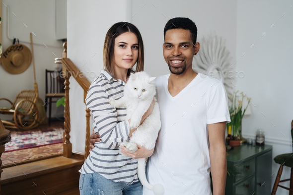 Happy young Caucasian pretty wife and African husband with cute cat animal - Stock Photo - Images