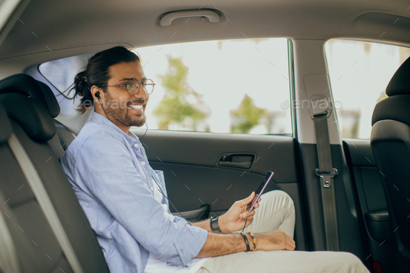 Middle-eastern man sitting at auto back seat, listening to music