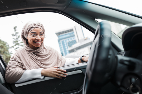 Happy attractive muslim afro american woman buyer looks into salon of new car from open window