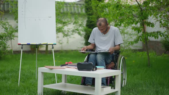 Concentrated Disabled Man Analyzing Business Graphs on Backyard Outdoors alt