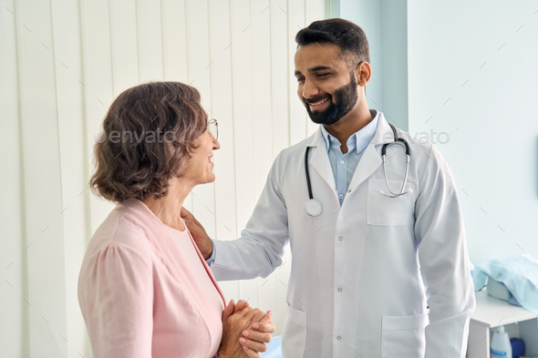 Cheerful Indian latin doctor consulting female older patient in hospital.